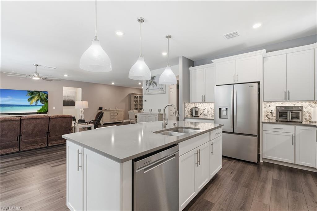 Modern kitchen featuring a central island with an undermount sink, pendant lighting, stainless steel appliances, and white cabinetry with a tile backsplash