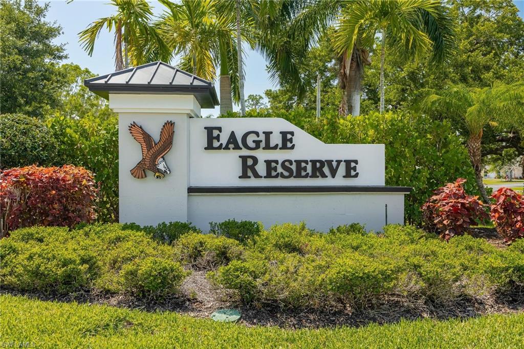 Community entrance signage with decorative cap, lush landscaping, and mature palm trees