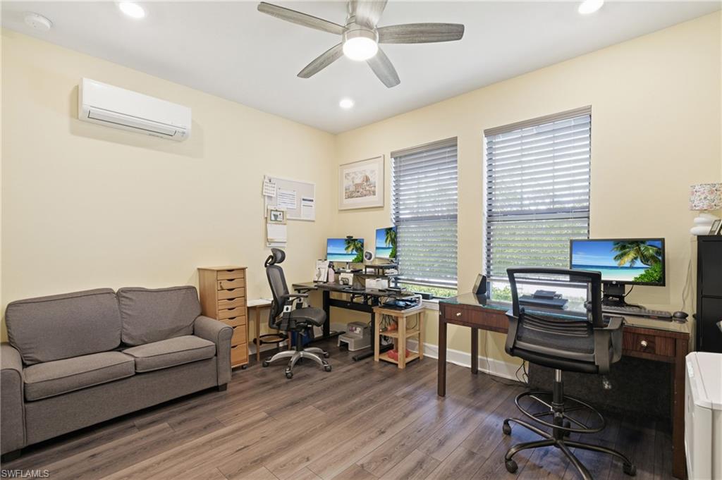 Recessed lighting, ceiling fan, two windows with blinds, wood-finish flooring, and a wall-mounted air conditioning unit
