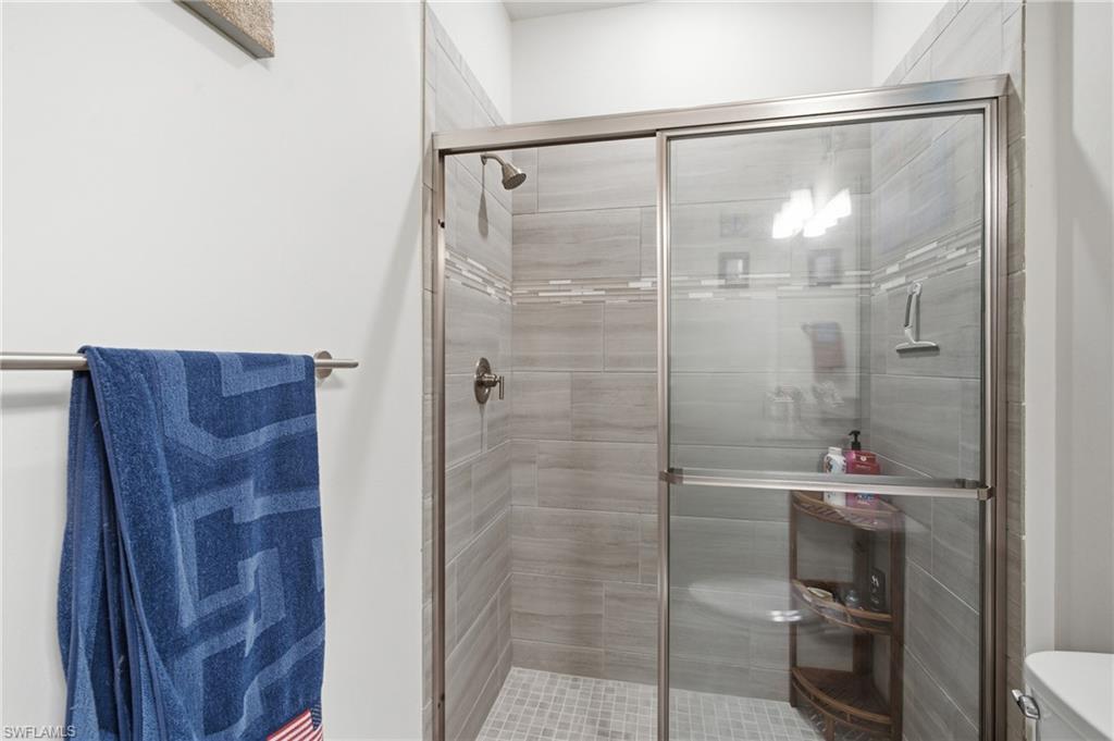 Shower enclosure with sliding glass doors, large format gray tile walls, decorative accent tile band, and a mosaic tile floor