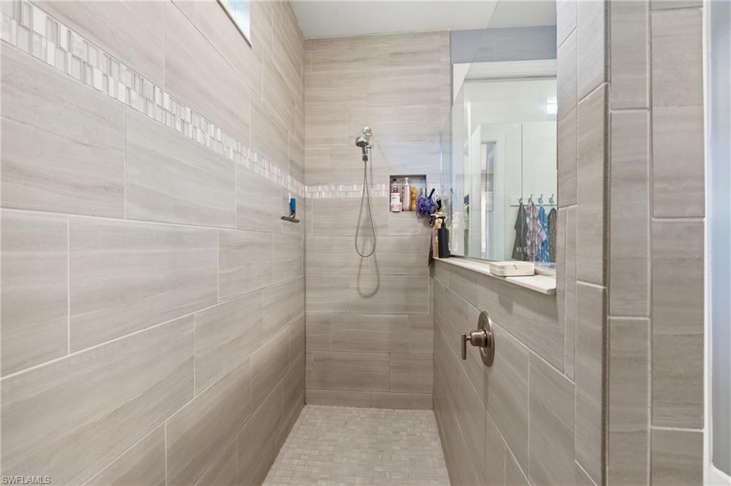 Tiled shower enclosure featuring a decorative accent band, built-in shelving, and a clear glass partition