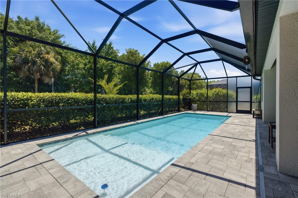 Screened enclosure with an in-ground swimming pool, paver deck, and mature landscaping