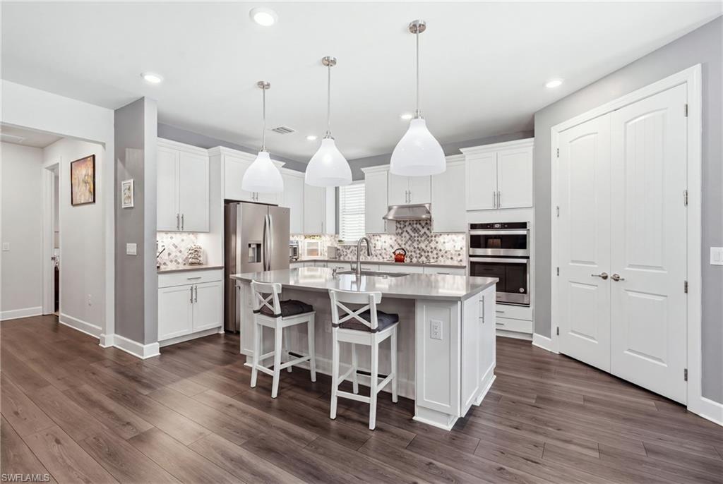 Kitchen featuring wood-finish flooring, a central island with countertop, white cabinetry, stainless steel appliances, and pendant lighting