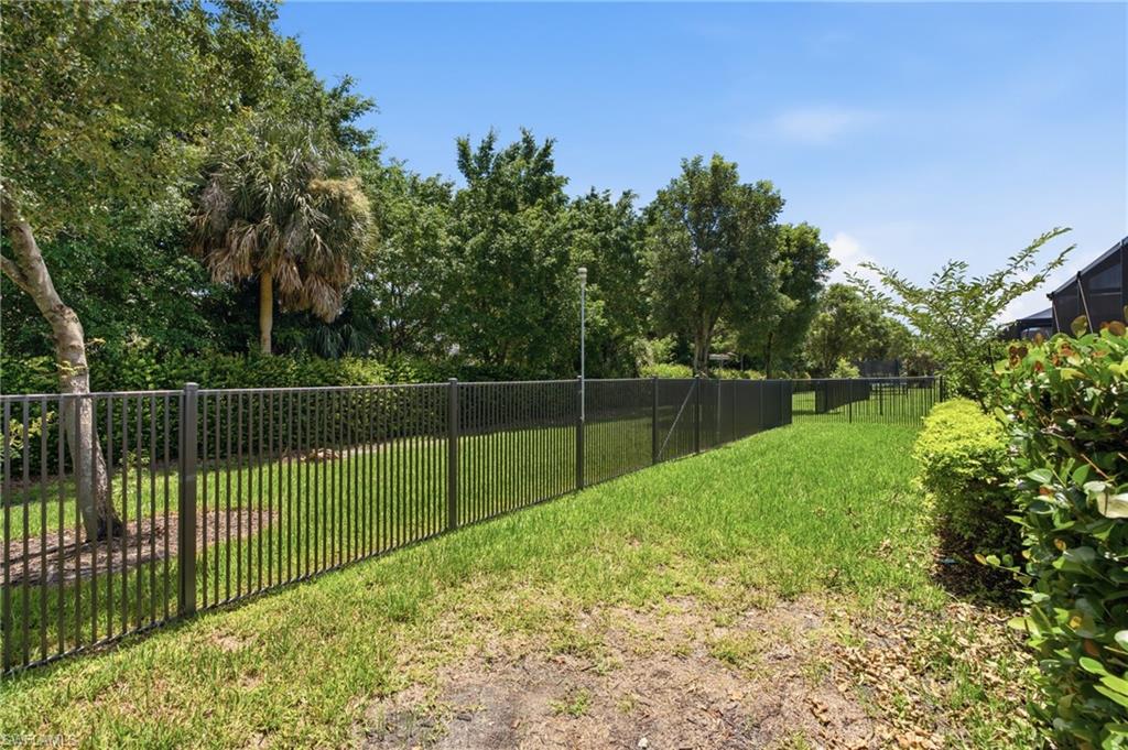 Expansive grassy area with a black aluminum fence, mature trees, and established shrubbery