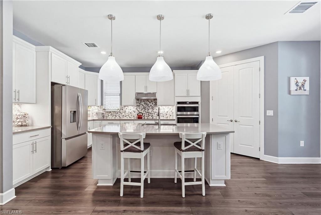 Kitchen featuring a central island, white cabinetry, integrated stainless steel appliances, pendant lighting, and wood-finish flooring
