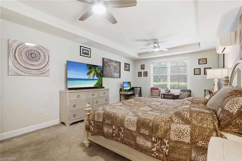 Tray ceiling with recessed lighting and two ceiling fans, carpeted flooring, wall-mounted split air conditioning unit, and built-in window blinds