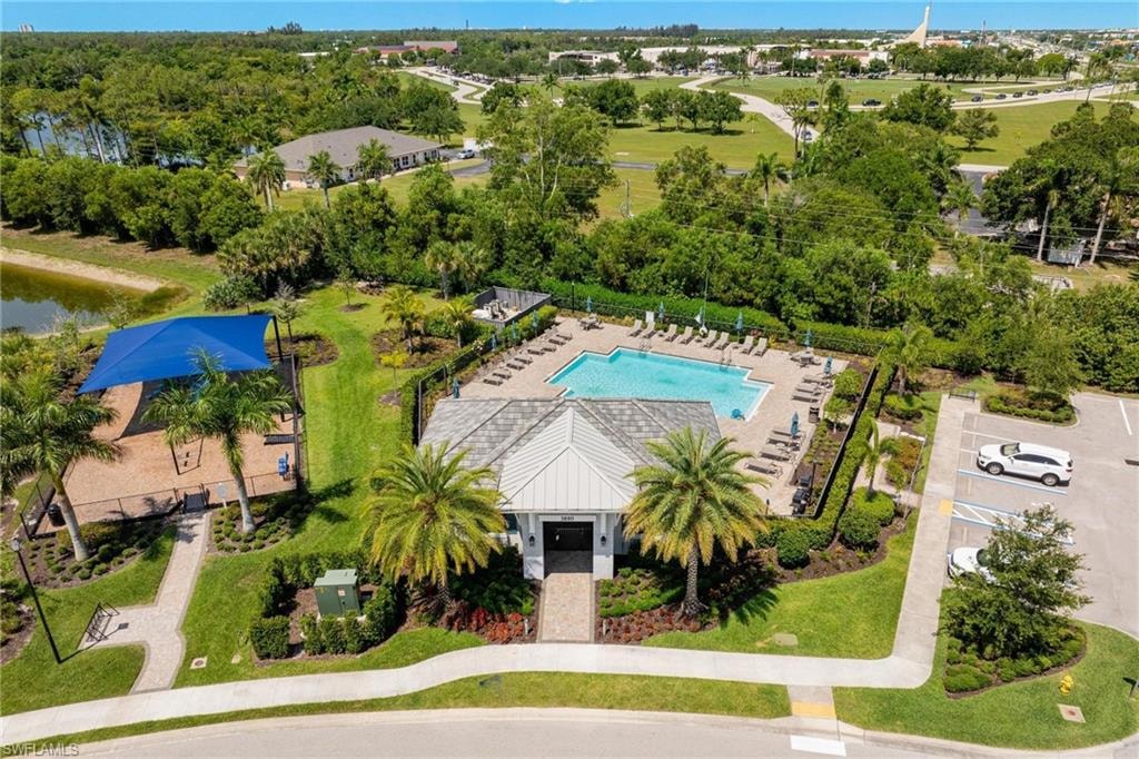 Resort-style pool with surrounding lounge chairs, covered outdoor seating area, adjacent building with covered entry, manicured green spaces, and a nearby structured playground with sunshade