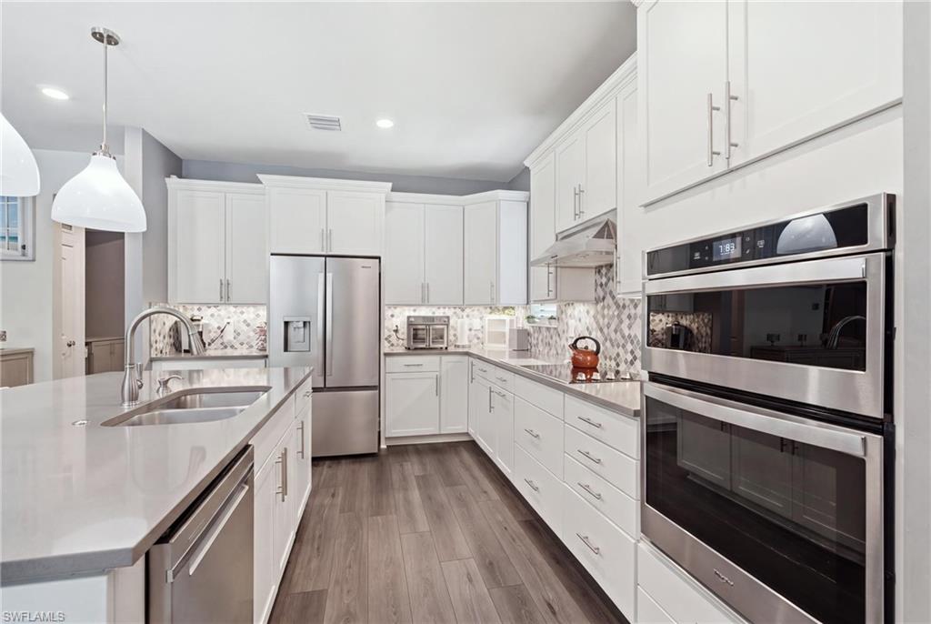 Kitchen featuring white cabinetry, stainless steel appliances, wood-finish flooring, and light-toned countertops