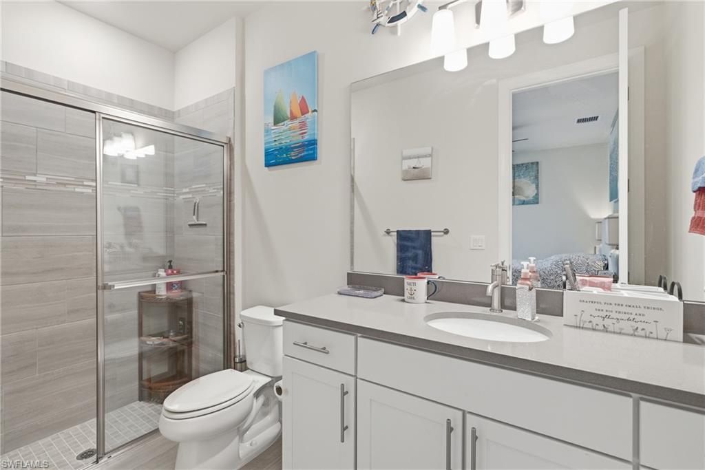Glass-enclosed shower with tile surround, single vanity with integrated sink, stone-finish countertop, and white cabinetry