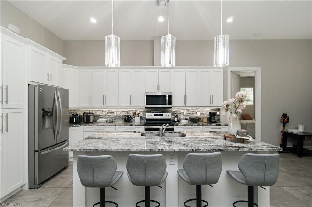 Kitchen featuring white cabinetry, stainless steel appliances, a large island with a stone countertop, and pendant lighting