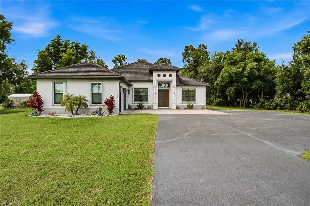 Stucco exterior with a tile roof, mature landscaping, and a wide paved driveway