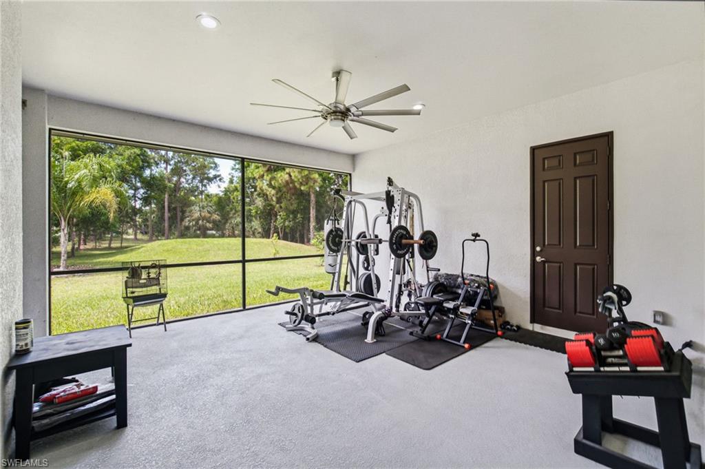 Screened enclosure with expansive backyard views, featuring a ceiling fan, recessed lighting, and a paneled exterior door