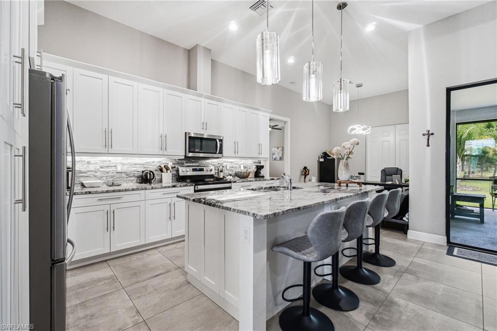 White shaker cabinetry with brushed nickel hardware, stainless steel appliances, granite countertops, tile backsplash, and three pendant lights above the island