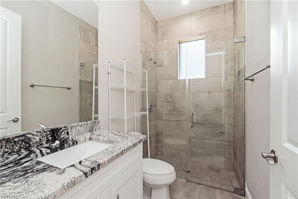 Spacious bathroom featuring a single vanity with stone countertop, large wall mirror, and an enclosed walk-in shower with tile surround and a transom window