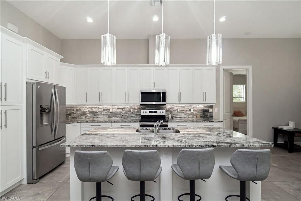 Spacious kitchen featuring an island with stone countertop, stainless steel appliances, white cabinetry, and a stacked stone backsplash