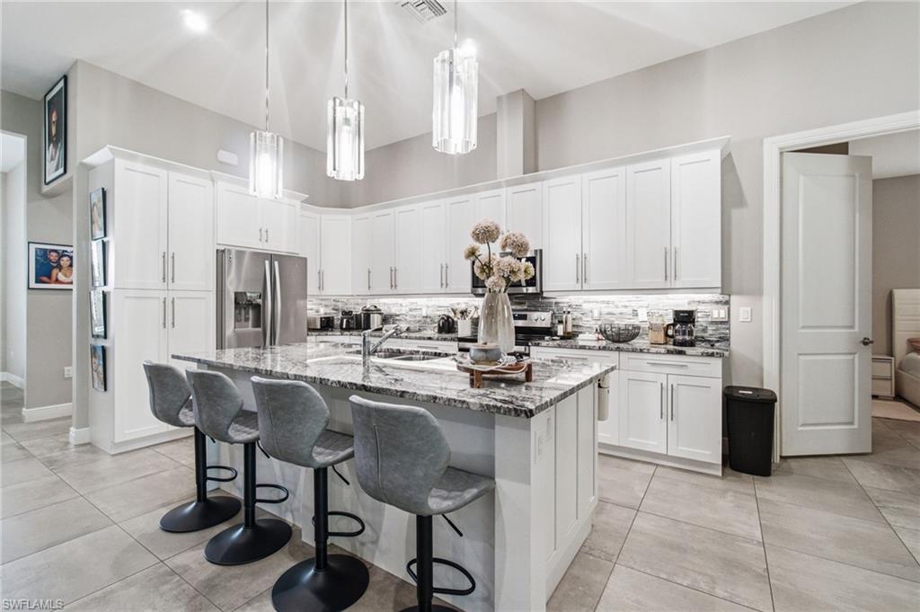 White shaker cabinetry, stainless steel appliances, speckled stone countertops, a tile backsplash, and large format tile flooring