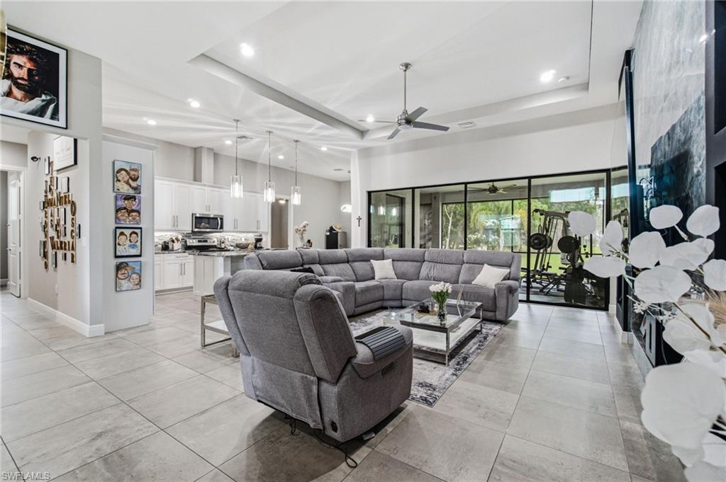 Open-concept living area featuring large format tile flooring, a tray ceiling with recessed lighting, and a modern ceiling fan