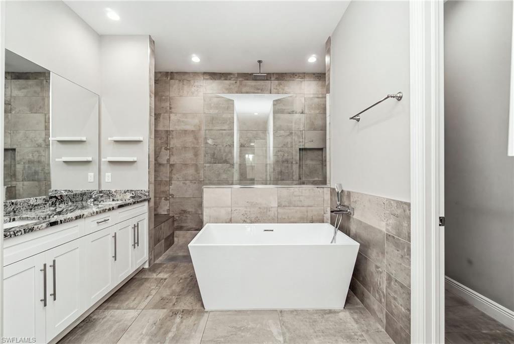 Dual vanity with granite countertops, tile flooring, freestanding soaking tub, frameless glass shower enclosure, and recessed lighting