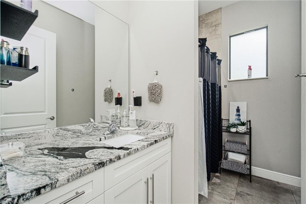 White vanity with a single basin, grey and white patterned countertop, and a large wall mirror
