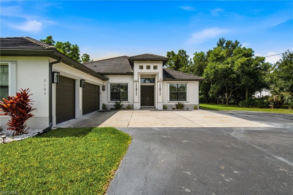 Contemporary stucco exterior, two-car garage, concrete driveway, tiled roof, and established landscaping
