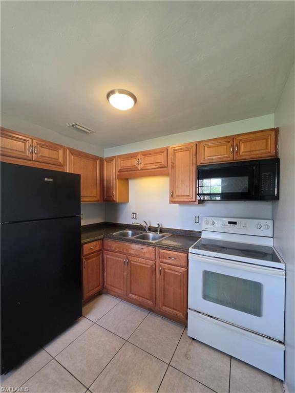 Kitchen featuring wood-finish cabinetry, a double basin sink, black countertops, and tile flooring