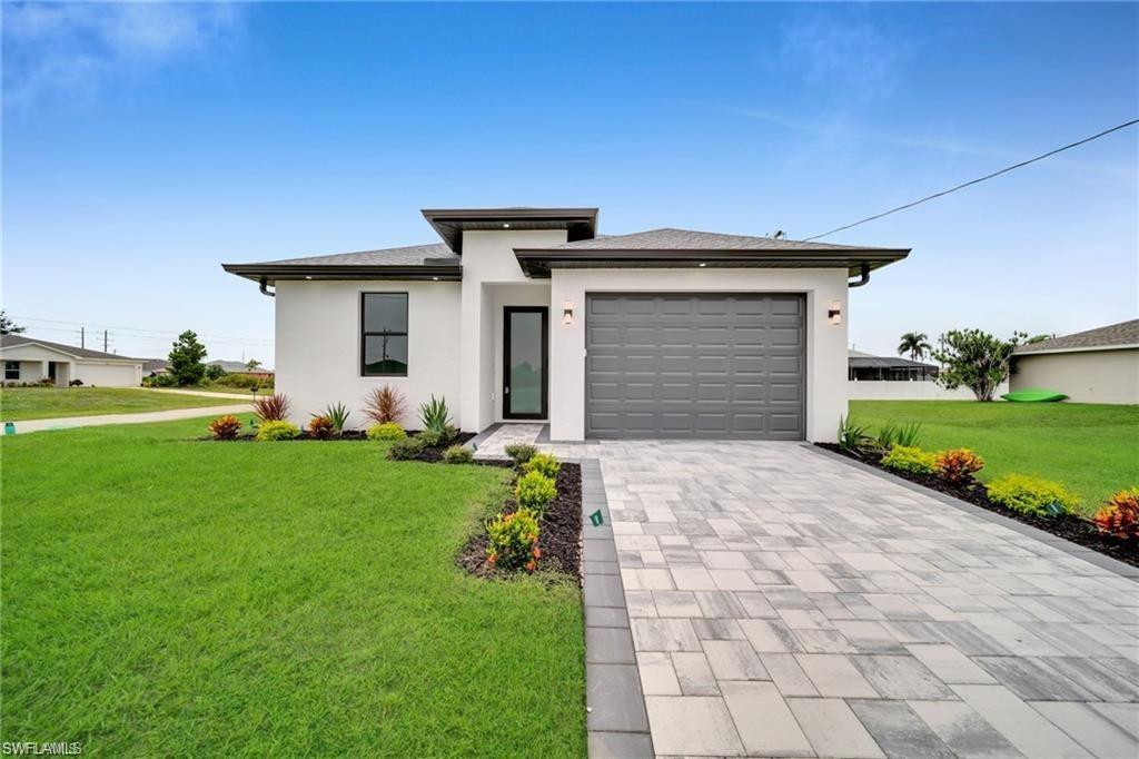 Modern stucco exterior with a gray garage door, paver driveway, and professional landscaping
