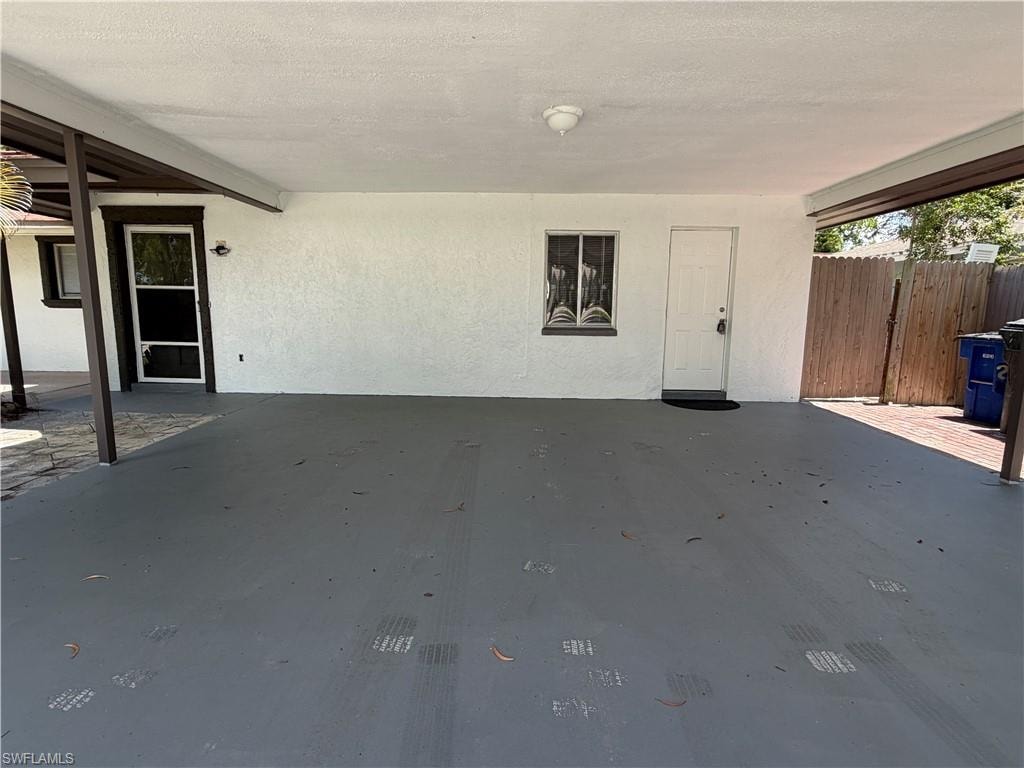 Covered carport with painted concrete flooring, stucco exterior, and a privacy fence