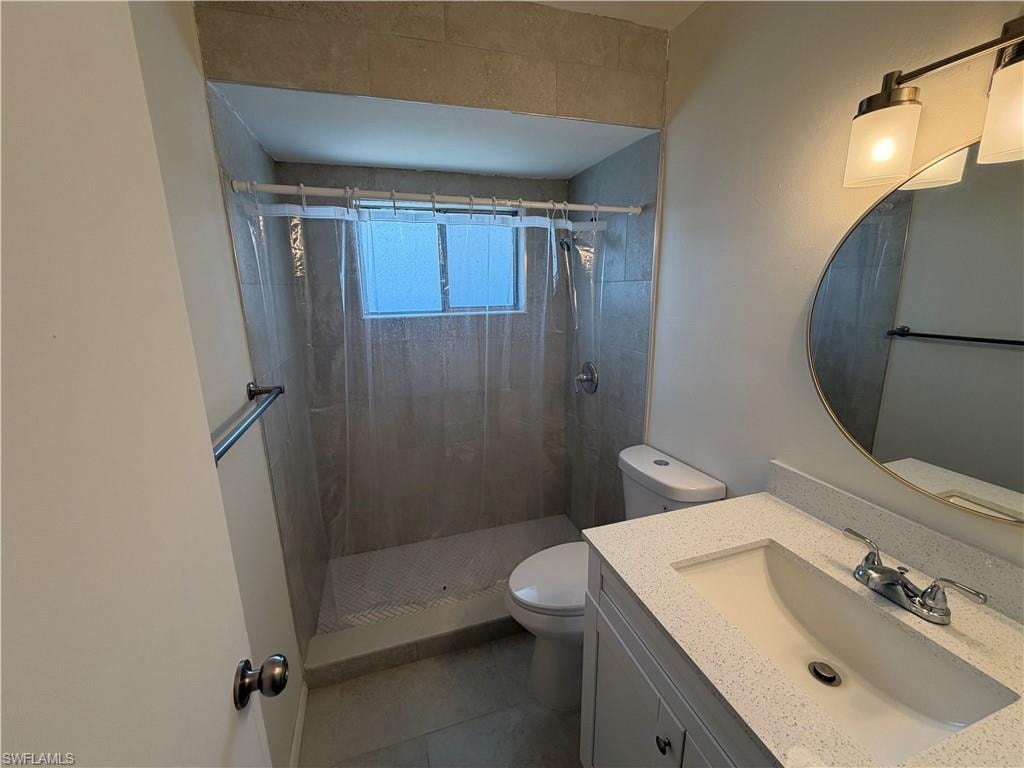 Bathroom featuring a tiled shower surround, integrated vanity with a single sink, round wall-mounted mirror, and overhead lighting fixture