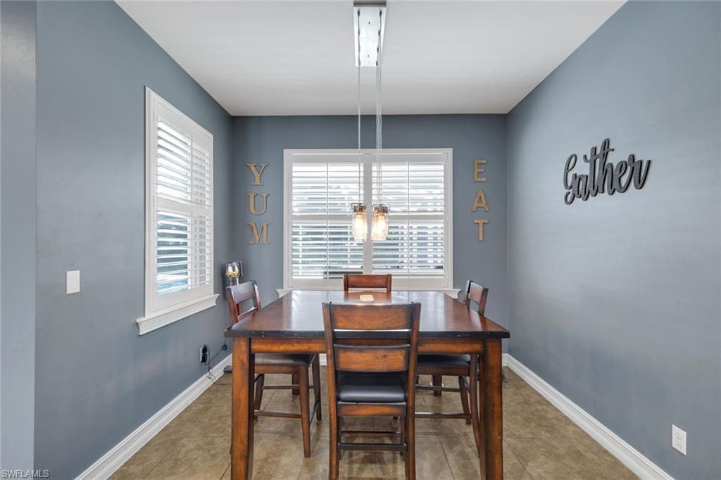 Recessed dining area with multiple windows, plantation shutters, a linear chandelier, and tile flooring