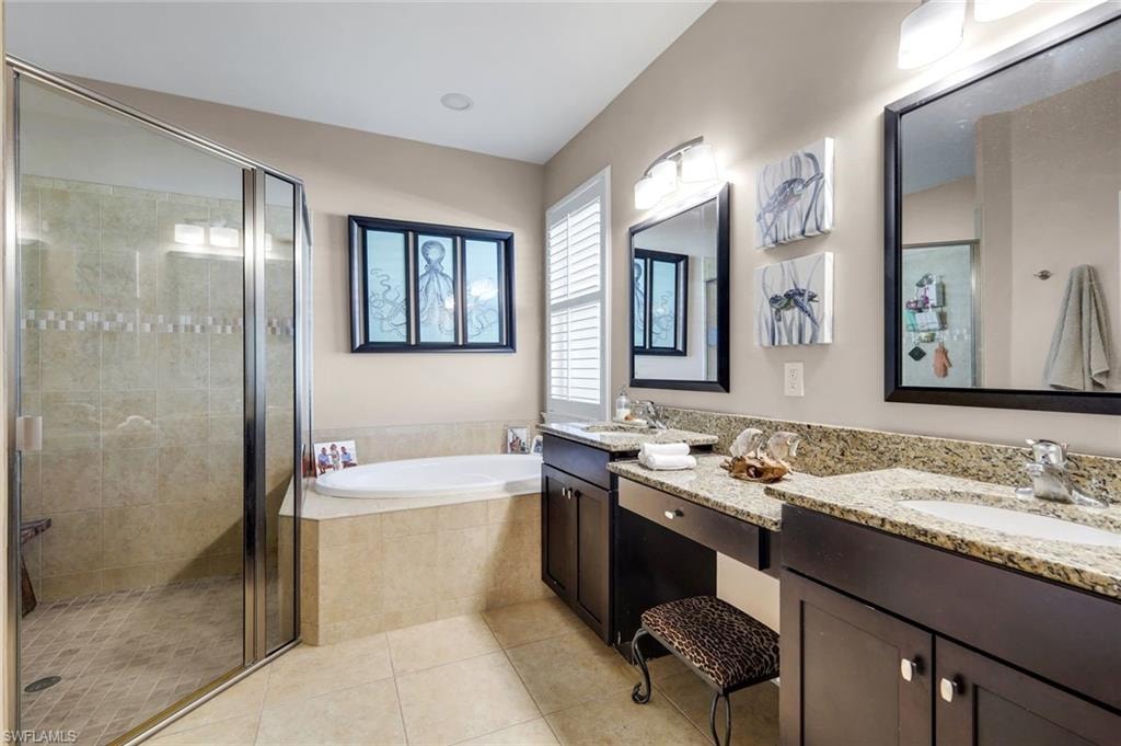 Spacious bathroom featuring a glass-enclosed shower, built-in soaking tub, dual vanities with granite countertops, and light-colored floor tiles