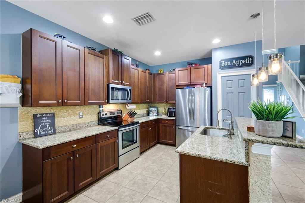 Contemporary kitchen featuring dark wood-finish cabinetry, light speckled countertops, stainless steel appliances, and a double basin sink