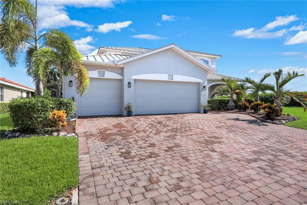 Two-car garage with individual doors, paver driveway, stucco exterior, decorative exterior lighting, and lush landscaping