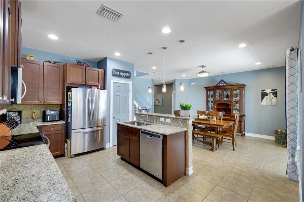 Open-concept kitchen featuring granite countertops, wood cabinetry, stainless steel appliances, and an eat-at island with pendant lighting