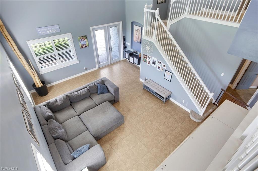 Two-story foyer with ceramic tile flooring, a prominent staircase with white railings, and double glass-panel doors
