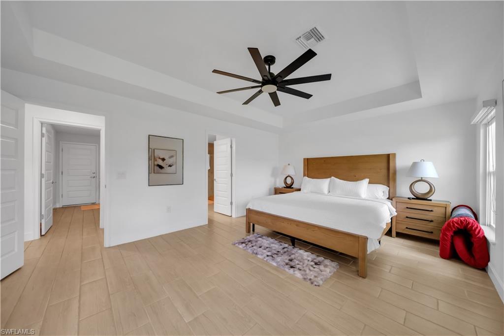 Tray ceiling with a ceiling fan, light wood-finish flooring, and natural light from a window with blinds