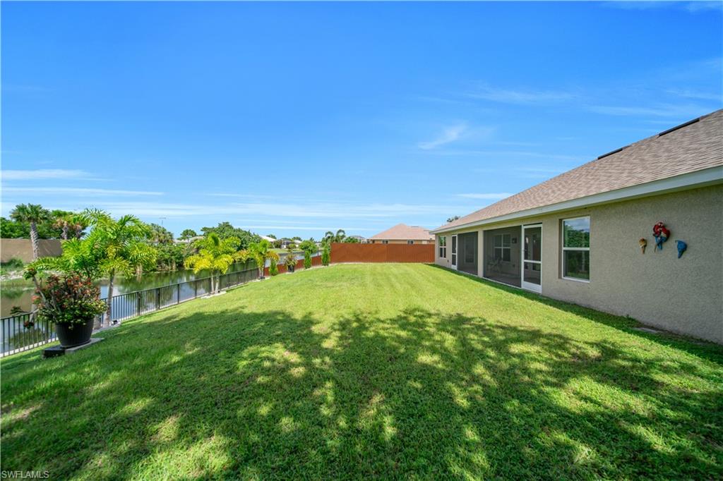 Expansive rear yard featuring a meticulously manicured lawn, mature landscaping with tropical plantings, waterfront access with railing, and a single-story residence with stucco exterior and composition shingle roofing visible along the property perimeter