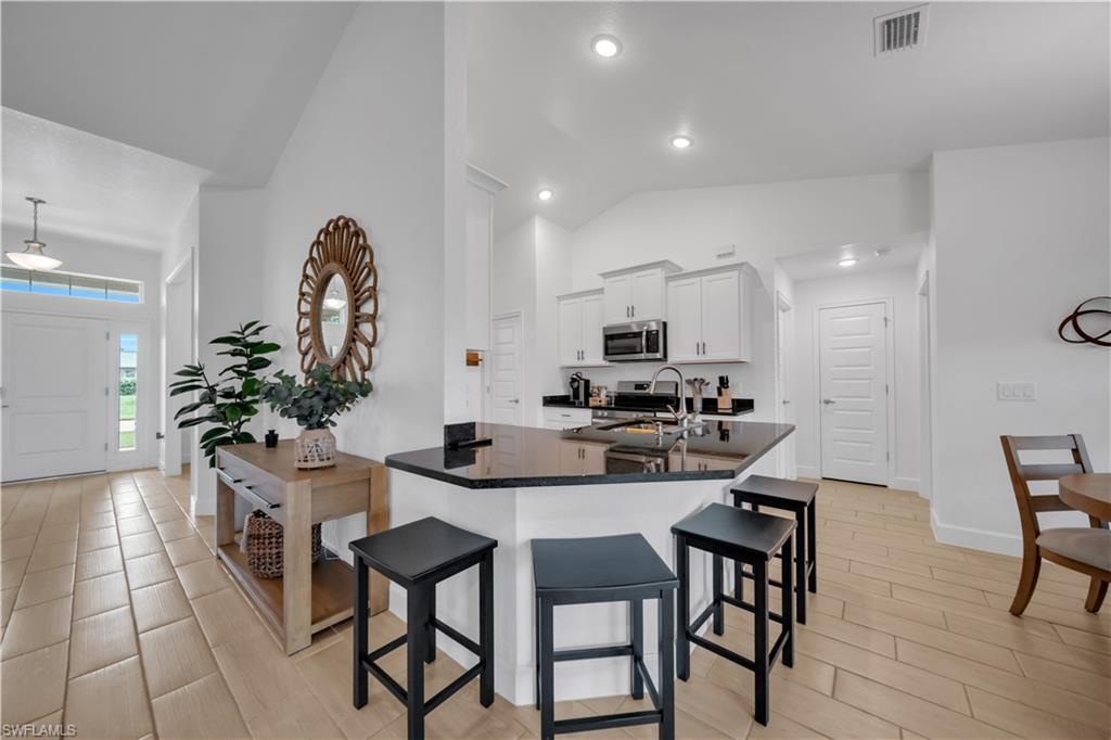 Vaulted ceiling, tile flooring, white shaker cabinetry, stainless steel appliances, and a kitchen island with dark countertops
