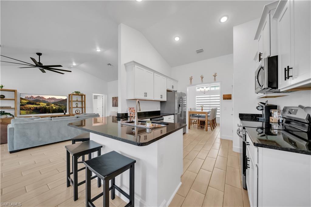 Vaulted ceilings with recessed lighting, an open-concept kitchen with dark countertops, white cabinetry with black hardware, and stainless steel appliances