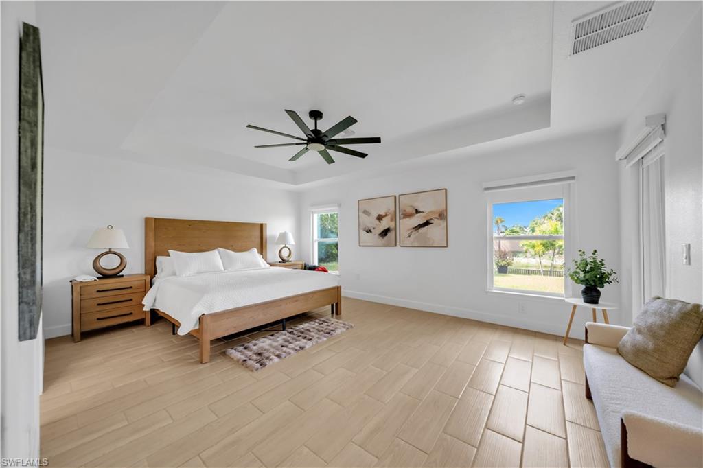 Tray ceiling with recessed lighting, wood-finish flooring, and multiple windows providing natural light