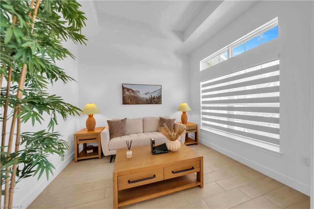 Tray ceiling, transom window, large window with horizontal blinds, light-toned tile flooring, and white walls