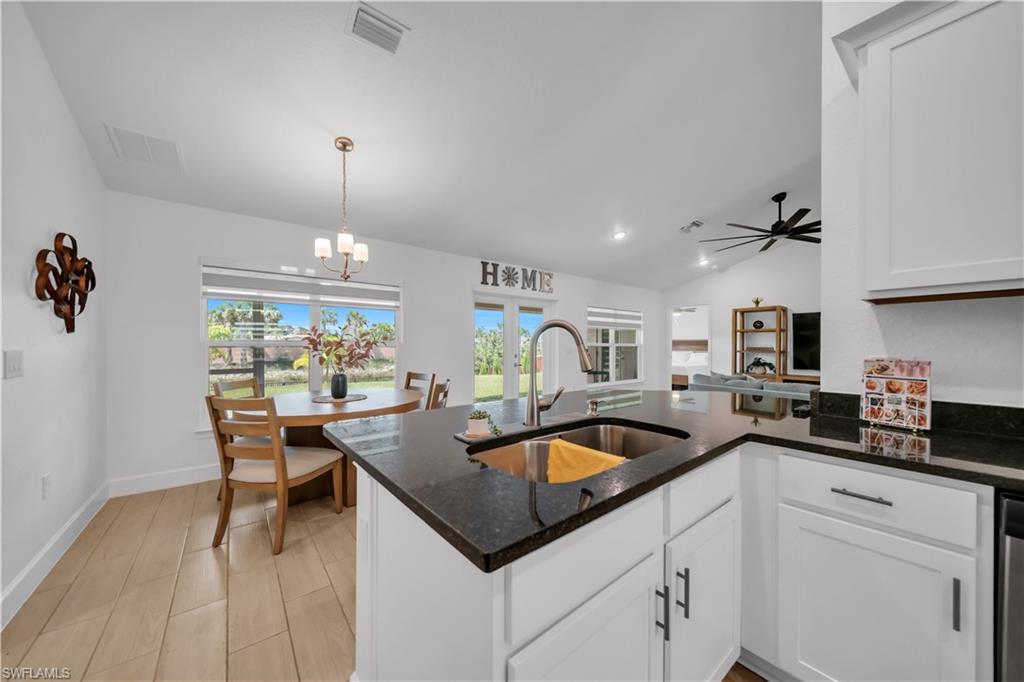 Kitchen island with a stainless steel sink and gooseneck faucet, white shaker cabinetry, dark countertops, and wood-finish flooring