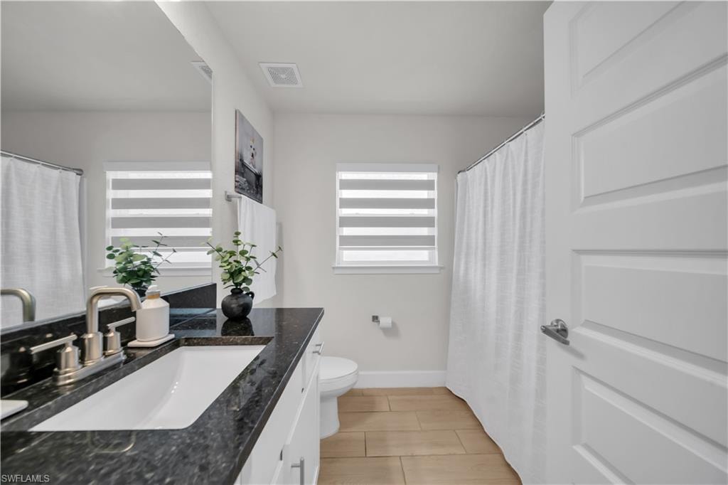 Vanity with dark countertop and undermount sink, brushed nickel faucet, large wall mirror, and wood-finish flooring