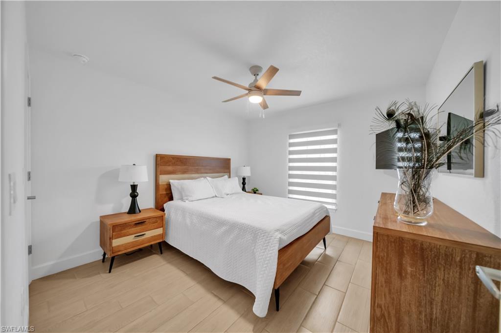 Wood-finish flooring, ceiling fan with integrated lighting, window with horizontal blinds, white wall finishes