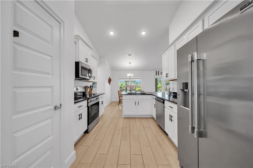 Kitchen featuring stainless steel appliances, white cabinetry, dark countertops, and wood-finish tile flooring
