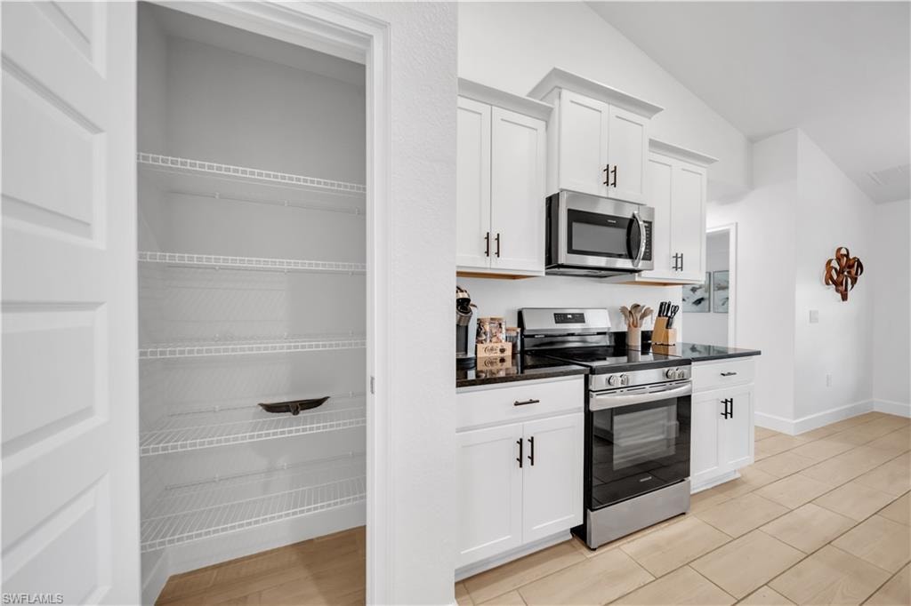 Kitchen featuring white cabinetry, dark countertops, stainless steel appliances, and a pantry with wire shelving