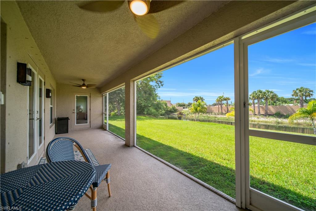 Screened patio with concrete flooring, two ceiling fans, and outdoor wall sconces, overlooking a manicured lawn and water feature