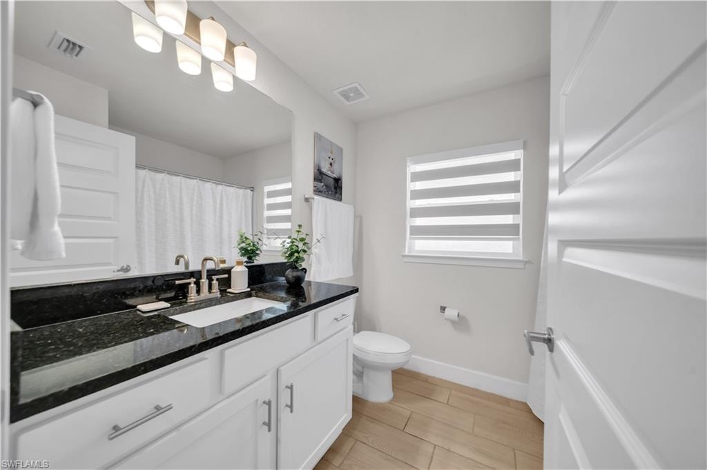 Vanity with a dark granite countertop and undermount sink, white cabinetry with brushed nickel hardware, and wood-finish tile flooring