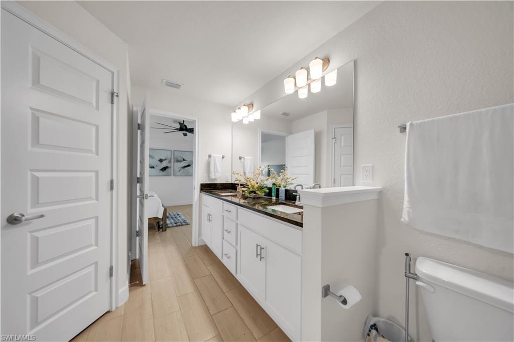 Double vanity with dark countertops, dual sinks, wood-finish flooring, and white cabinetry