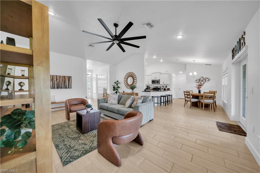 Vaulted ceilings, wood-finish flooring, a modern black ceiling fan, recessed lighting, and a kitchen with white cabinetry