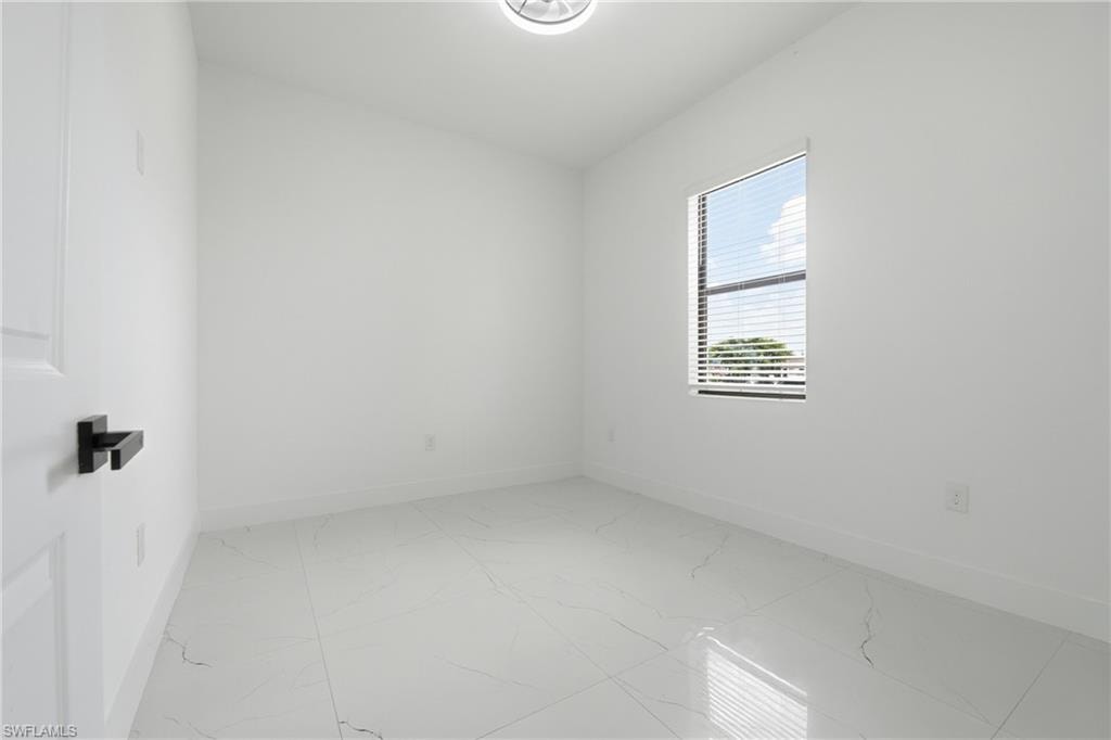 Bright white walls with a single window, white tile flooring, and a white paneled door with a black lever handle